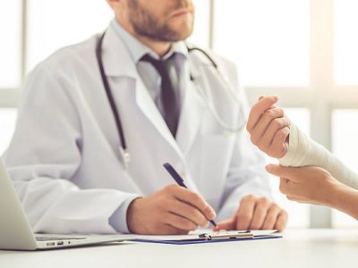 Cropped image of handsome medical doctor listening to female patient with damaged hand and making notes while working in his office